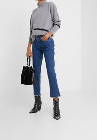 Pull gris à col montant avec une rayure marine, associé  à un jean bleu taille haute. Bottines noires cloutées et sac seau noir.