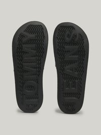 Solas de sapatos de borracha preta com "TOMMY" e "JEANS" embutidos, com padrões de solado zig-zag para tração. Textura suave por todo o lado.