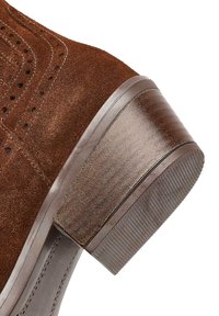 Brązowy zamszowy but z teksturowanym wykończeniem, z okrągłym noskiem i piętą w stylu drewnianym z delikatnymi poziomymi rowkami.