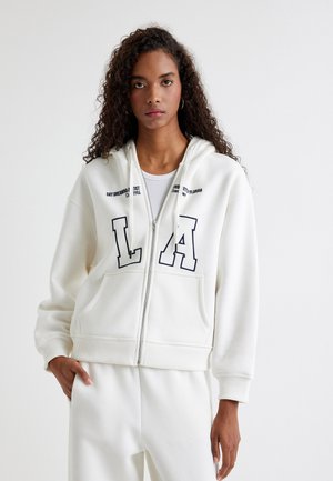 Witte rits hoodie van zachte stof, met marineblauwe "LA" letters op de voorkant, grote zakken en een capuchon met trekkoorden.