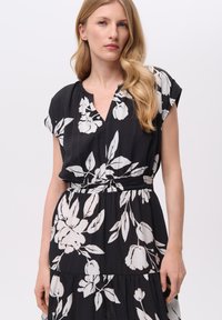 Czarna sukienka z białym kwiatowym wzorem, z rękawami typu cap, dekoltem w serek i elastycznym pasem, wykonana z lekkiego materiału o miękkiej teksturze.