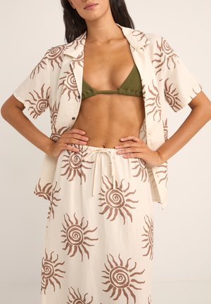 Conjunto de camisa y falda de lino con un fondo crema y motivos de sol en marrón. La camisa tiene un corte relajado y la falda incluye una cintura con cordón.