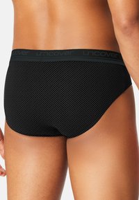 Sort underbukse i brief-stil med et tekstureret diamantmønster, med en ensfarvet sort linning markeret med "uncover" i grå.