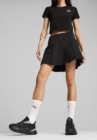 Outfit con crop top nero e gonna plissettata, dal design sportivo. Abbinato a sneakers nere e calzini alla caviglia bianchi, con dettagli del logo.