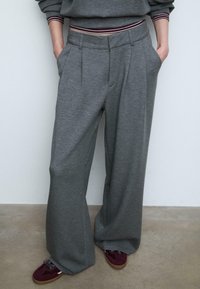 Szare szerokie spodnie w miękkim materiale, z plisami z przodu i kieszeniami bocznymi, połączone z bordowymi i beżowymi sneakersami.