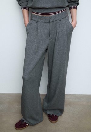 Szare szerokie spodnie w miękkim materiale, z plisami z przodu i kieszeniami bocznymi, połączone z bordowymi i beżowymi sneakersami.