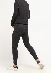 Vaqueros skinny negros elásticos de tiro alto, con bolsillos traseros, combinados con una sudadera negra y zapatillas blancas.