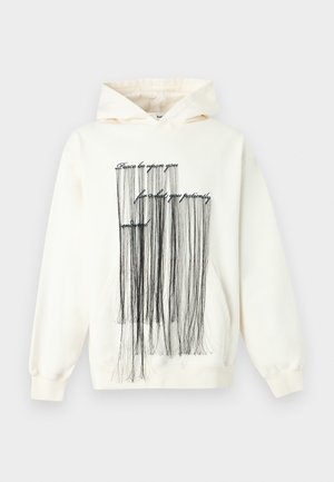Cream hoodie with black fringe strands hanging from cursive text reading "Peace be upon you for what you patiently endured."