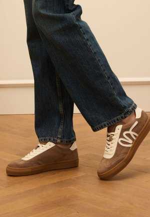 Bruine nubuck sneakers met crème accenten en witte veters. Rubberen zool. Draag ze met donkerblauwe jeans, die een relaxte pasvorm en een rafelige zoom laten zien.