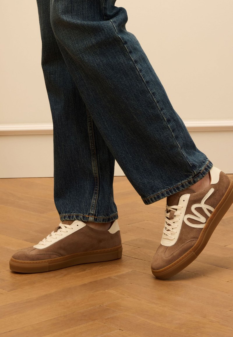Bruine nubuck sneakers met crème accenten en witte veters. Rubberen zool. Draag ze met donkerblauwe jeans, die een relaxte pasvorm en een rafelige zoom laten zien.