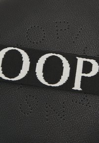 Borsa in pelle nera con texture, dotata di una prominente tracolla intrecciata nera caratterizzata da grandi lettere bianche. Dettaglio in rilievo notevole sulla superficie.