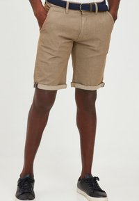 Beige, textured shorts with rolled cuffs and side pockets, paired with a navy woven belt. Black sneakers complete the look.