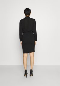 Blusa negra con rayas verticales, de mangas largas, combinada con una falda negra de longitud a la rodilla. Lleva puestas botas de tacón negro hasta el tobillo.