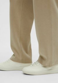 Beiga sweatpants med en slät textur och sid sömsdetaljer, kombinerade med vita sneakers med rund tå och texturerad sula.