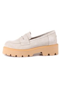 Mocassins en daim beige avec une semelle plateforme épaisse et texturée de couleur marron clair, présentant une bride unique sur le cou-de-pied et un design à bout arrondi.