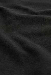 Tela negra con una textura suave, que muestra ligeras ondas y pliegues, indicando un material ligero y elástico.