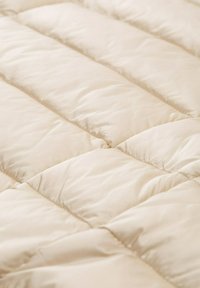 Couverture en beige matelassé avec une texture douce et lisse, présentant des sections surélevées régulièrement espacées et un éclat subtil sur la surface du tissu.