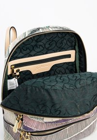 Interior de mochila de tela estampada con forro verde, bolsillo con cremallera beige y herrajes dorados. Incluye un compartimento principal espacioso.