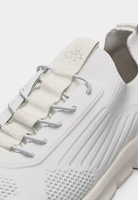 Κοντινή λήψη λευκού αθλητικού παπουτσιού με υφασμάτινο πλεκτό ύφασμα, ελαστικά κορδόνια και υφασμάτινο λουράκι στην κορυφή με την ετικέτα "MOP".