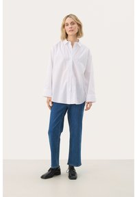 Witte button-up shirt met een kraag, lange mouwen en een relaxte pasvorm, gecombineerd met blauwe rechttoe-rechtaan jeans en zwarte veterschoenen.