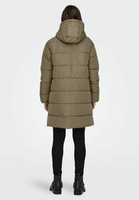 Khaki foret jacket med hætte, der har et quiltet design og en hofte-længde skæring. Parret med sorte tætsiddende bukser og ankelstøvler.