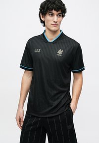 Μαύρη αθλητική φανέλα με κατακόρυφες λεπτές ρίγες, αντίθετο τουρκουάζ κολάρο και ανάγλυφες λεπτομέρειες λογότυπου. Κατασκευασμένη από ελαφρύ ύφασμα για άνεση.