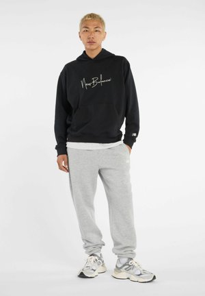 Felpa nera con logo bianco, pantaloni sudati grigi e sneakers multicolori. La felpa presenta una tasca frontale e una vestibilità comoda.