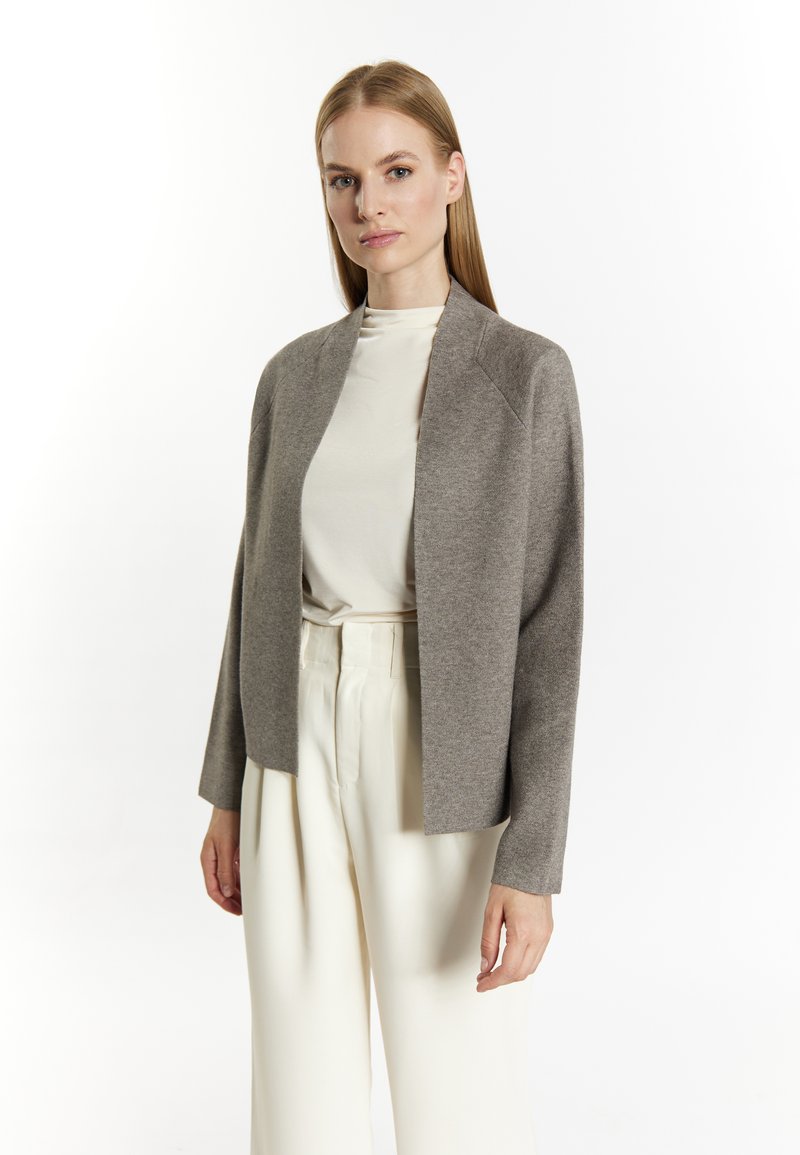 Cardigan gri deschis cu față deschisă și mâneci lungi, realizat dintr-un material moale. Asortat cu un pulover crem cu guler înalt și pantaloni albi cu talie înaltă.