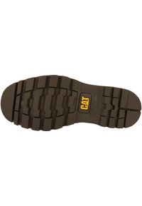 Suela de bota de goma marrón con huellas profundas y resistentes, que presenta un logo de CAT. La superficie texturizada proporciona agarre y durabilidad.