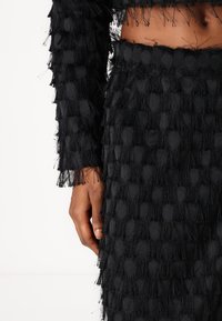 Black textured outfit with fringed accents, featuring a layered bobble pattern. The fabric is soft with a tactile, dimensional quality.