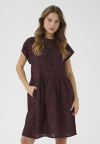 Robe florale bordeaux à manches courtes, avec un bouton sur le devant et des poches latérales. Tissu léger avec un design ample et à volants.