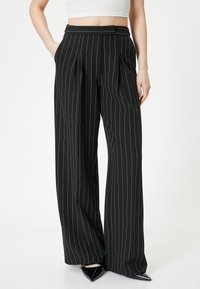 Pantalons larges noirs avec des rayures blanches verticales, devant plissé, passants de ceinture et poches, fabriqués en tissu léger.