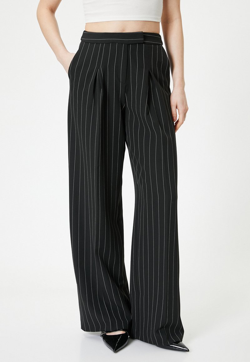 Pantalons larges noirs avec des rayures blanches verticales, devant plissé, passants de ceinture et poches, fabriqués en tissu léger.