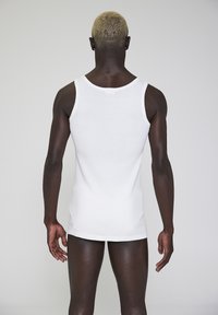 White sleeveless tank top made of soft fabric, form-fitting design, plain texture, with a rear tag and a straight hem.