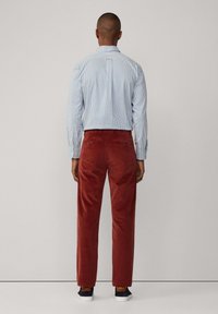 Pantalones de corduroy rojos con un corte recto, combinados con una camisa abotonada a rayas en azul y blanco. Zapatillas oscuras completan el atuendo.