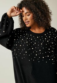 Maglione nero dalla vestibilità ampia, con un motivo di perle bianche di varie dimensioni sul davanti. Tessuto a maglia strutturato con maniche larghe.