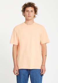Ferskenfarvet bomulds T-shirt med korte ærmer, rund hals og en afslappet pasform. Bæres med blå denim jeans. Ingen synlige mønstre eller logoer.