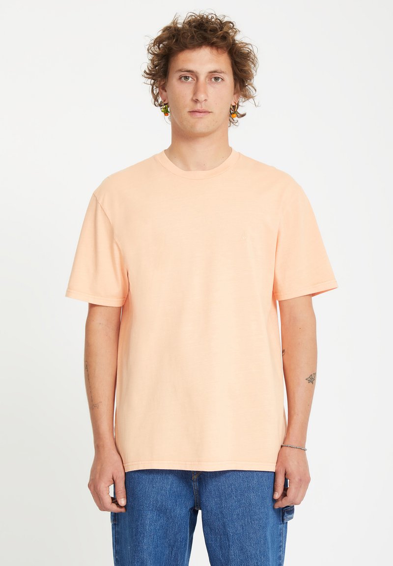 Ferskenfarvet bomulds T-shirt med korte ærmer, rund hals og en afslappet pasform. Bæres med blå denim jeans. Ingen synlige mønstre eller logoer.