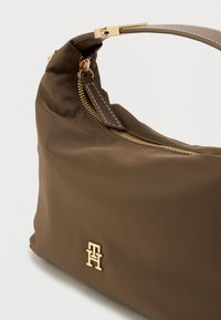 Olivengrønn nylon skulderveske med teksturert overflate, detaljer i gulltone, topp glidelås, og en fremtredende merkevarelogo på siden.