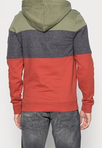 Sudadera con capucha con un diseño de bloques de color que presenta secciones en verde oliva, azul marino y óxido. Material de algodón suave con un ajuste relajado.