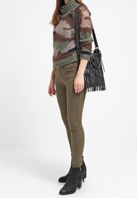 Neulepaita, jossa on korkea kaulus, ja siinä on maanläheisiä sävyjä esittävä camouflagemalli. Oliivinvihreät kapeat housut ja mustat nilkkasaappaat. Hapsullinen laukku.