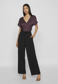 Satinai bordo spalvos viršus su gilia V formos iškirpte, derinamas su juodomis plačiomis kelnėmis, turinčiomis raištelio juosmenį ir šonines kišenes.