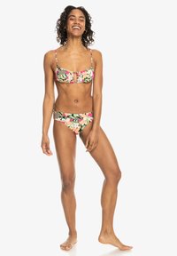 Bikini set met een bloemenpatroon in roze, groen en beige. De top heeft dunne bandjes en een sleutelgatdetail; de onderkant is low-rise.