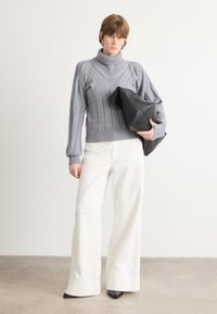 Svetlo siva turtleneck pulover z rebrasto teksturo, kombiniran z belimi širokimi hlačami in črno torbico. Gladki materiali in strukturiran dizajn.