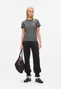 Woman wearing black and white striped t-shirt, black joggers, black loafers, and holding a black handbag with pink keychain.
