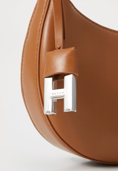 Ruskea nahkainen käsilaukku, jossa on hopeanvärinen metallinen "H"-logo, sileä pinta, kaareva muoto ja hihna, joka on kiinnitetty nahka-askin ympärille.