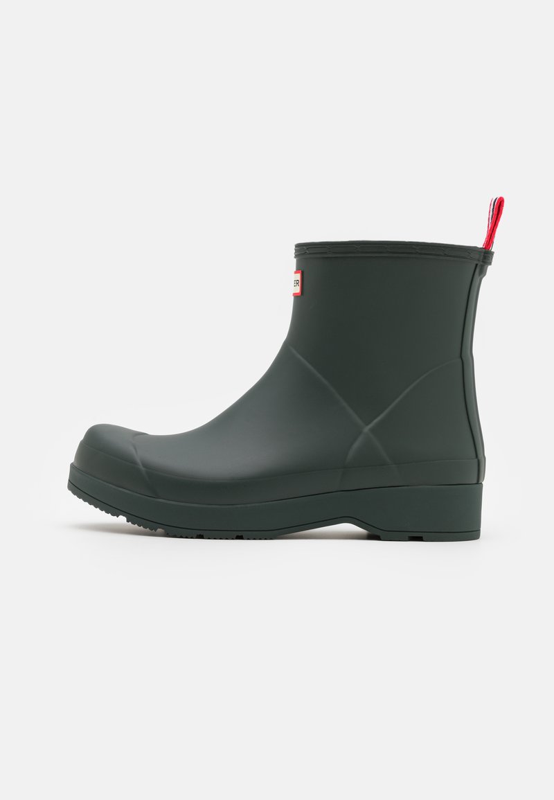 Green rubber ankle boot with a smooth surface, rounded toe, and a red pull tab. Features a textured sole for grip.