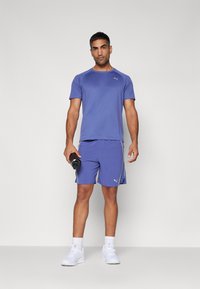 T-shirt e calções de atletismo leves em azul escuro, com corte slim e logótipo PUMA, combinados com uma garrafa de água preta e sneakers brancos.