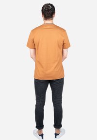 Korte mouwen, rondhals oranje T-shirt van katoen, gecombineerd met donkere spijkerbroeken en witte sneakers. Geen zichtbare logo's of patronen.