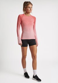 Langærmet sportstop i gradient nuancer af pink, med et tætsiddende design og glat tekstur, kombineret med sorte shorts og sneakers.